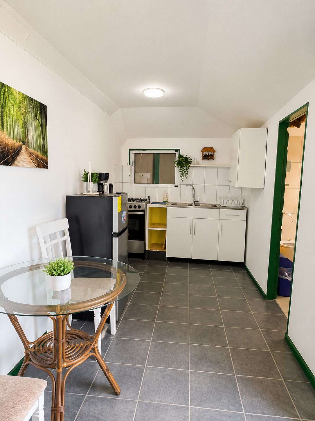 A compact kitchen with white cabinets, a dining table with chairs, and a small window.