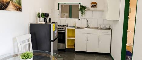 A compact kitchen with white cabinets, a dining table with chairs, and a small window.