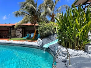 A swimming pool with clear blue water, surrounded by tropical plants and a stone wall. - Rancho El Sobrino (Sabana Westpunt)