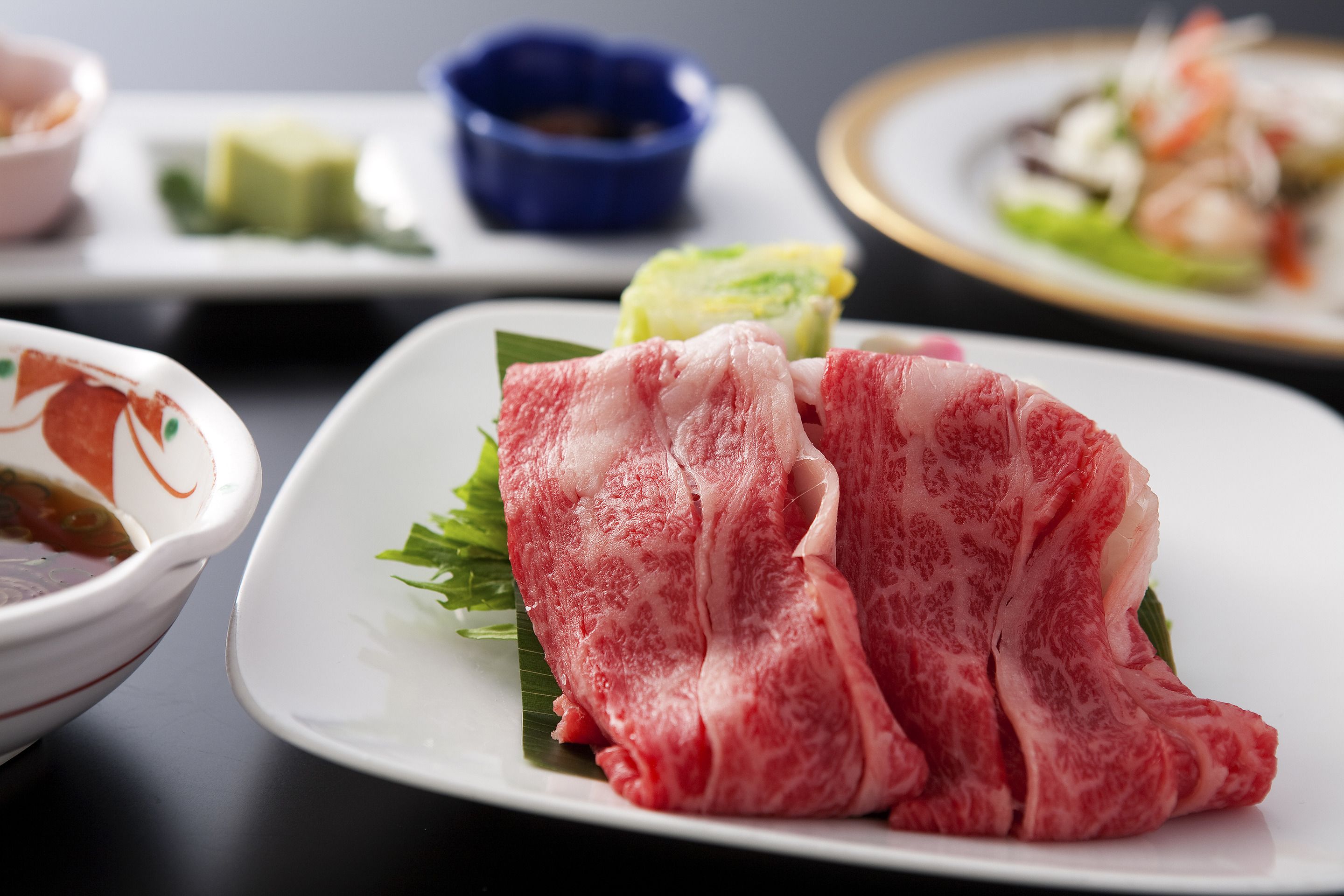 Un tavolo da pranzo con diversi piatti, tra cui un piatto di carne cruda, una ciotola di zuppa e una piccola ciotola blu.