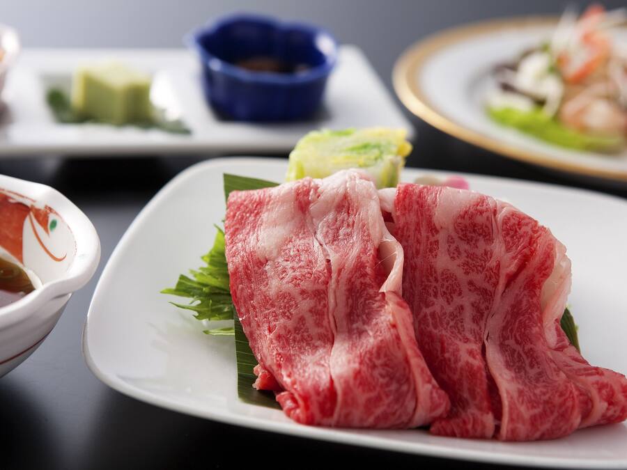 Un tavolo da pranzo con diversi piatti, tra cui un piatto di carne cruda, una ciotola di zuppa e una piccola ciotola blu.