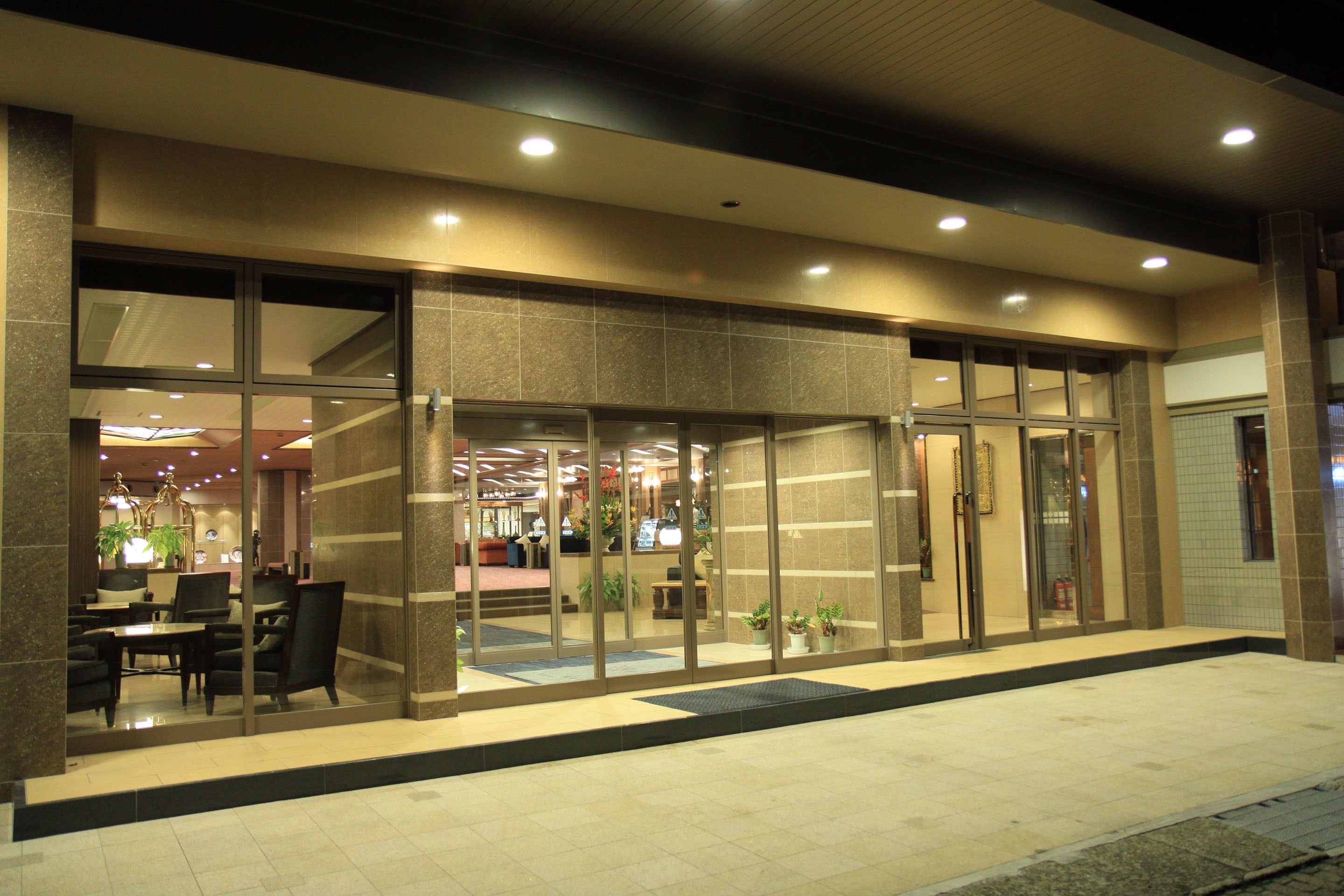 A hotel entrance with a glass door, a reception desk, and a seating area with chairs and tables.