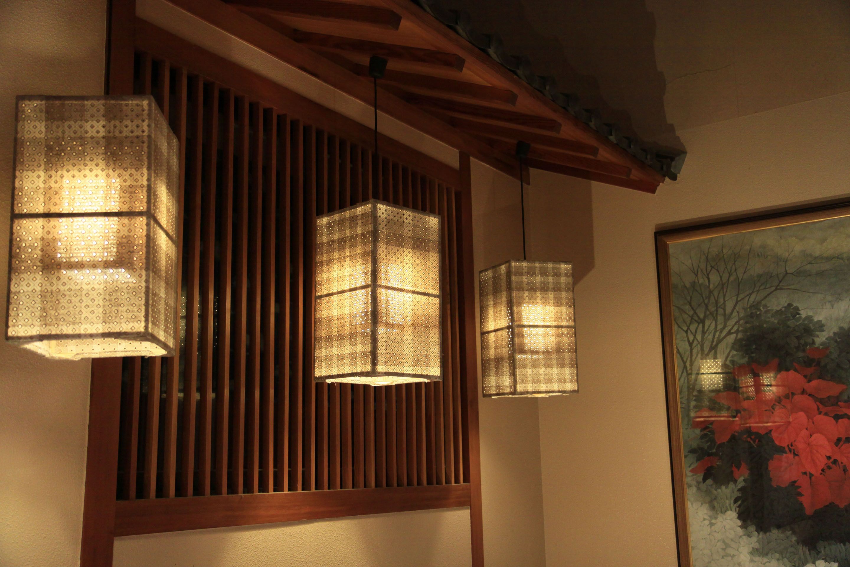 A room with wooden slats, hanging paper lanterns, and a framed painting of red foliage.