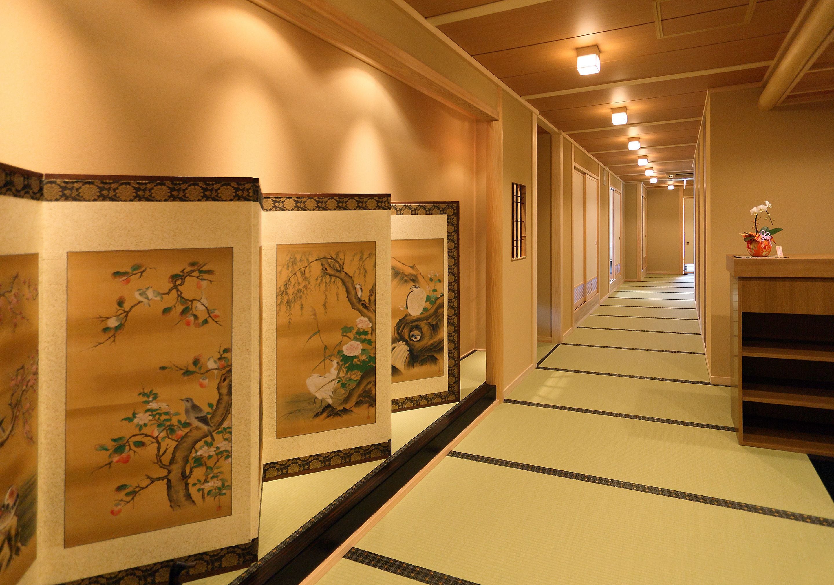 Un pasillo con suelo de tatami, pinturas tradicionales japonesas en las paredes y un mostrador de recepción con un jarrón de flores.
