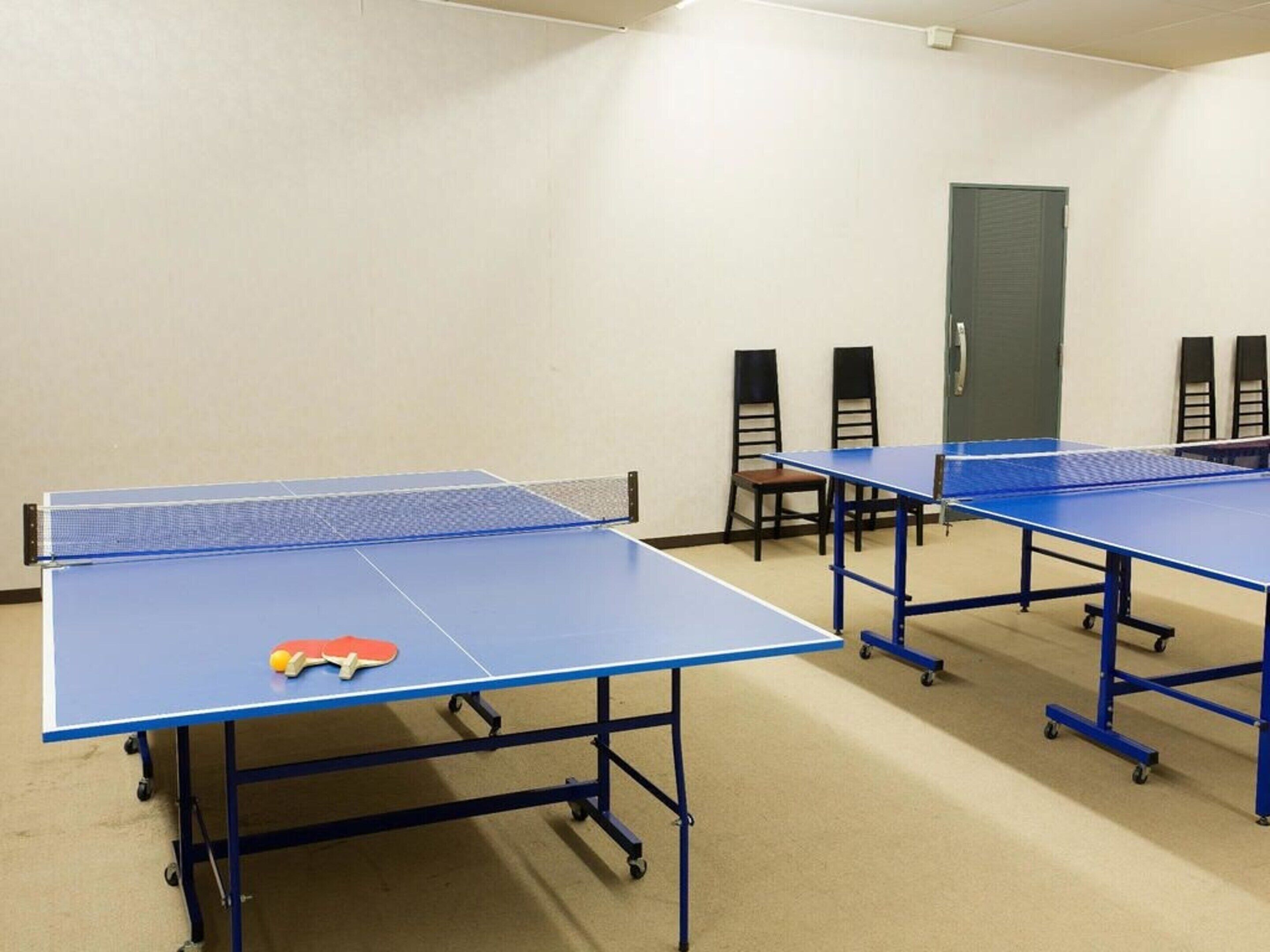 A room with multiple ping pong tables, chairs, and a door.