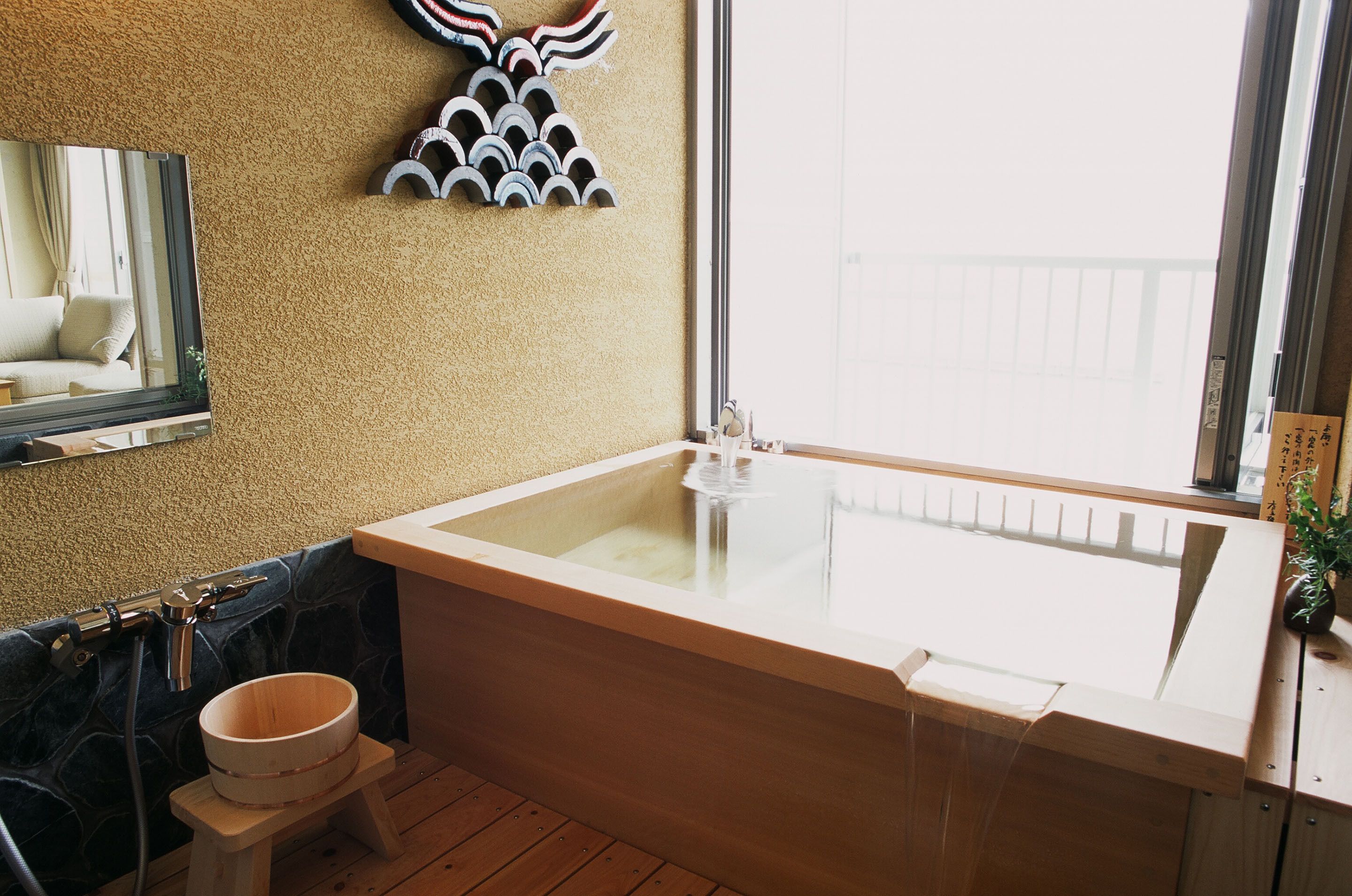 A bathroom with a bathtub, a wooden stool, a mirror, and a window.