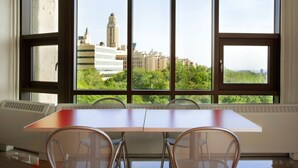 A room with a large window overlooking a cityscape, a wooden table, and two wicker chairs. - ZUM Auberge d'été - Résidences de l'Université de Montréal (Montreal)