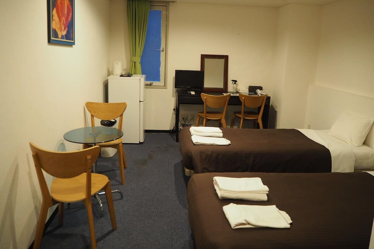 Une chambre d’hôtel avec deux lits, un bureau, une chaise, un petit réfrigérateur et une télévision.