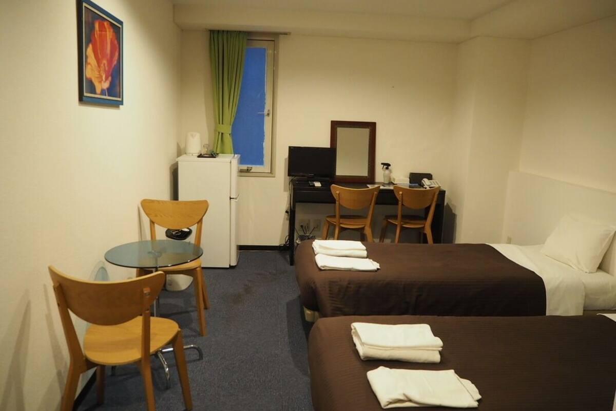 Une chambre d’hôtel avec deux lits, un bureau avec un ordinateur, une chaise, une petite table et une fenêtre avec des rideaux.