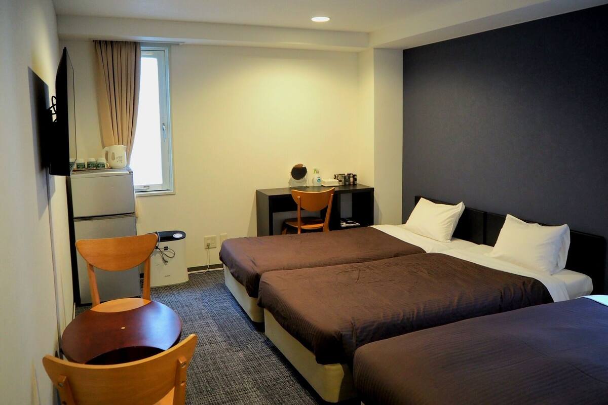 Une chambre d’hôtel avec deux lits, un bureau, une chaise, une télévision et une fenêtre avec des rideaux.