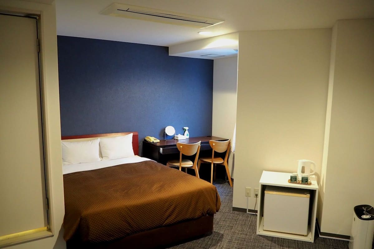 Une chambre d’hôtel comprenant un lit, un bureau, une chaise, une petite table avec une machine à café et une poubelle.