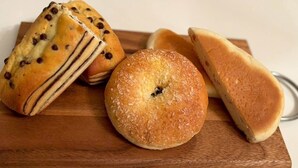 Une planche en bois sur laquelle sont disposées trois pâtisseries : un muffin aux pépites de chocolat, un muffin nature et une pâtisserie ronde avec un trou au centre.