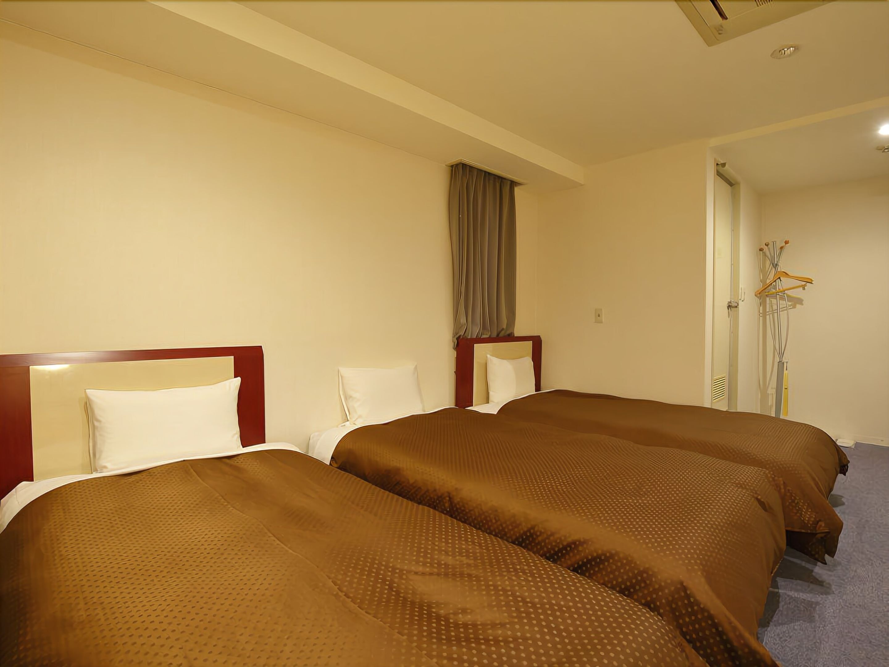 Una habitación de hotel con dos camas, una ventana con cortinas y un perchero con perchas.
