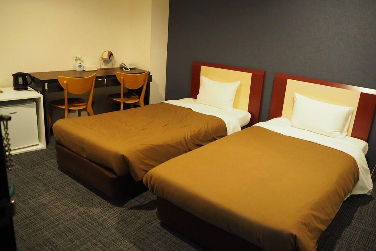 Une chambre d’hôtel avec deux lits, un bureau, une chaise, un petit réfrigérateur et un téléphone fixé au mur.