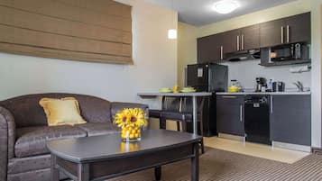 A compact living space with a sofa, coffee table, and a kitchen area including a microwave and refrigerator.