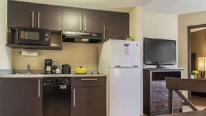Cocina compacta con microondas, refrigerador, cafetera y un televisor pequeño.