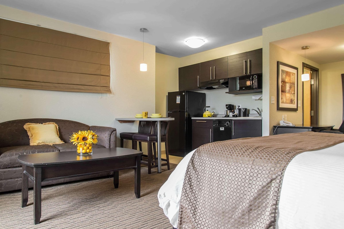 A compact hotel room with a sofa, a small dining table, a kitchenette, and a bed.