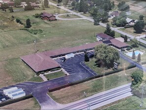 An aerial view of a motel with a large parking lot, a swimming pool, and a building with a red roof.
