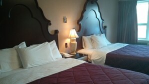 Ein Hotelzimmer mit zwei Betten, beide mit weißen Leinen und einer dunkelroten Decke. Am linken Bett steht eine Nachttischlampe, auf dem Nachttisch ein Telefon.