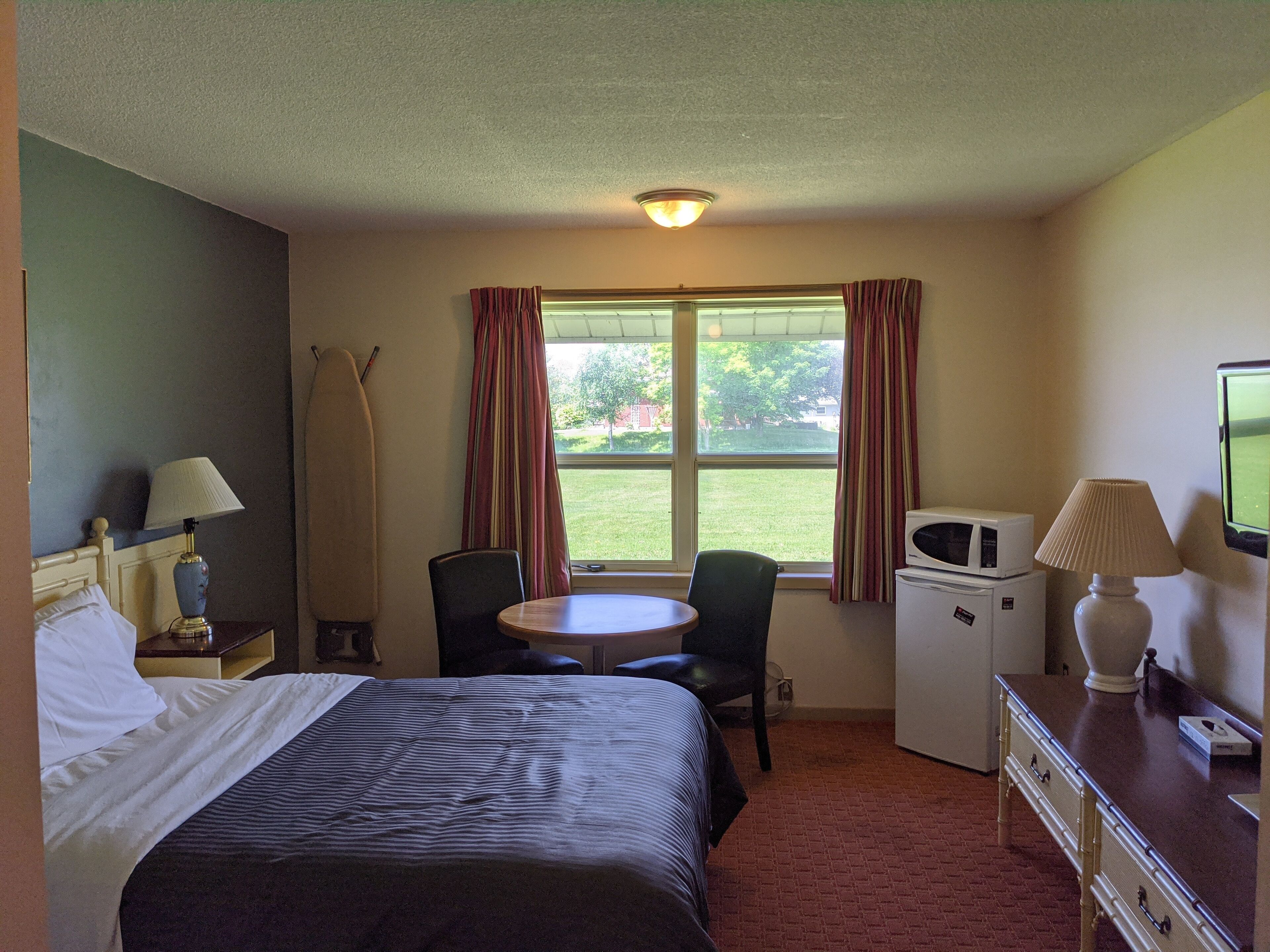 Una habitación de hotel con cama, escritorio, silla, microondas y televisor.