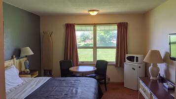 Una habitación de hotel con cama, escritorio, silla, microondas y televisor.
