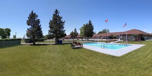 A swimming pool with lounge chairs, surrounded by a grassy area and tall trees.