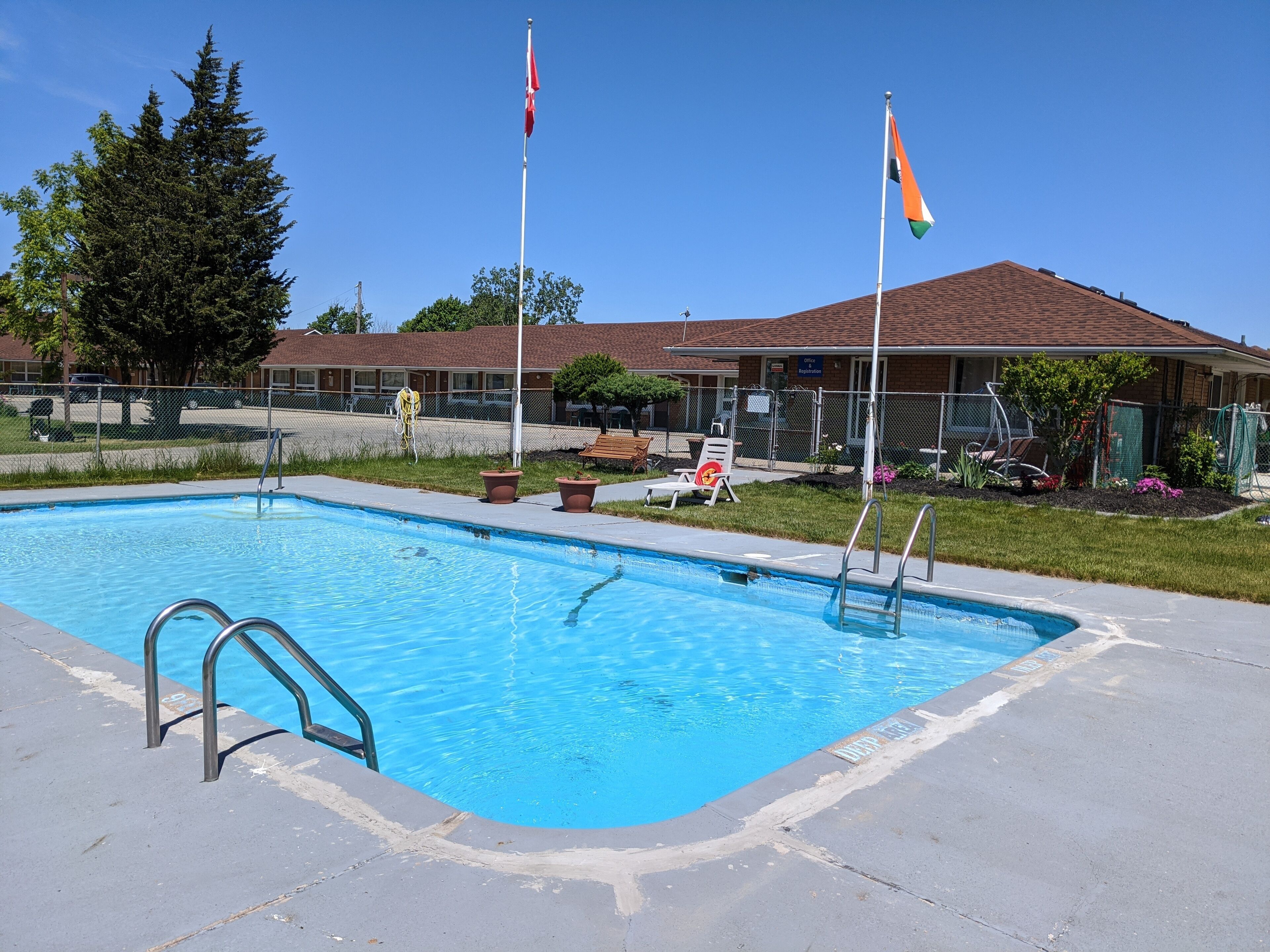 A swimming pool with metal ladders, surrounded by a fenced area with lounge chairs and a building in the background.