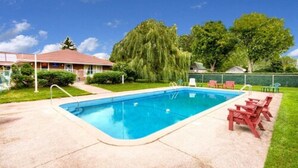 Ein rechteckiger Swimmingpool mit einer Leiter an einer Seite, umgeben von einer Betonplattform. Entlang des Beckenrandes befinden sich rote Liegestühle.