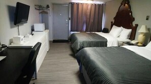 A hotel room with two beds, a desk with a chair, a television, and a small table with a lamp.