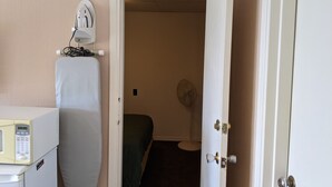 Ein Hotelzimmer mit einem Bett, einem Nachttisch mit Mikrowelle, einem Ventilator und einer Tür zu einem weiteren Raum.