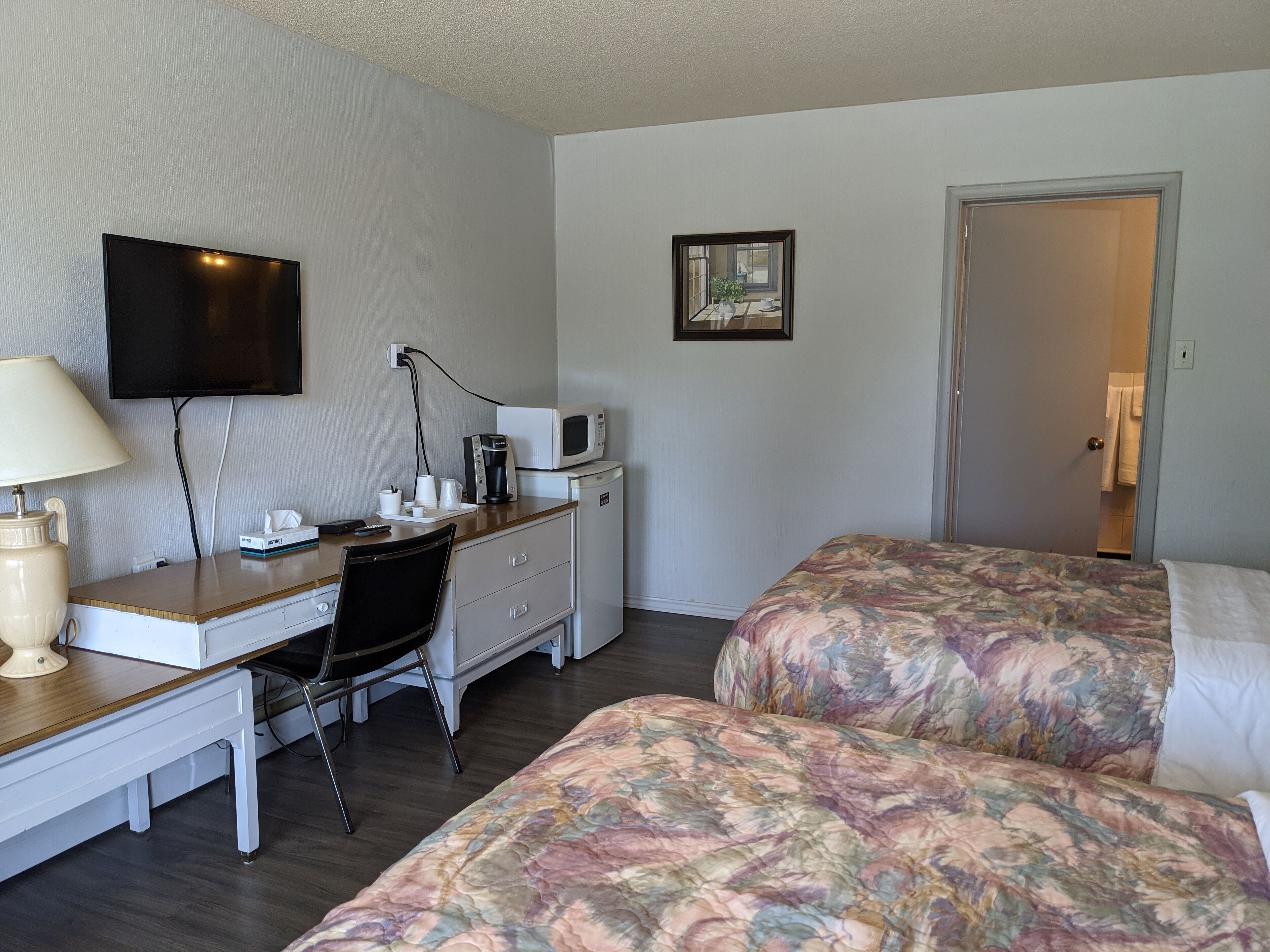 A hotel room with a desk, a chair, a bed with floral bedding, a television, a microwave, and a door leading to a bathroom.