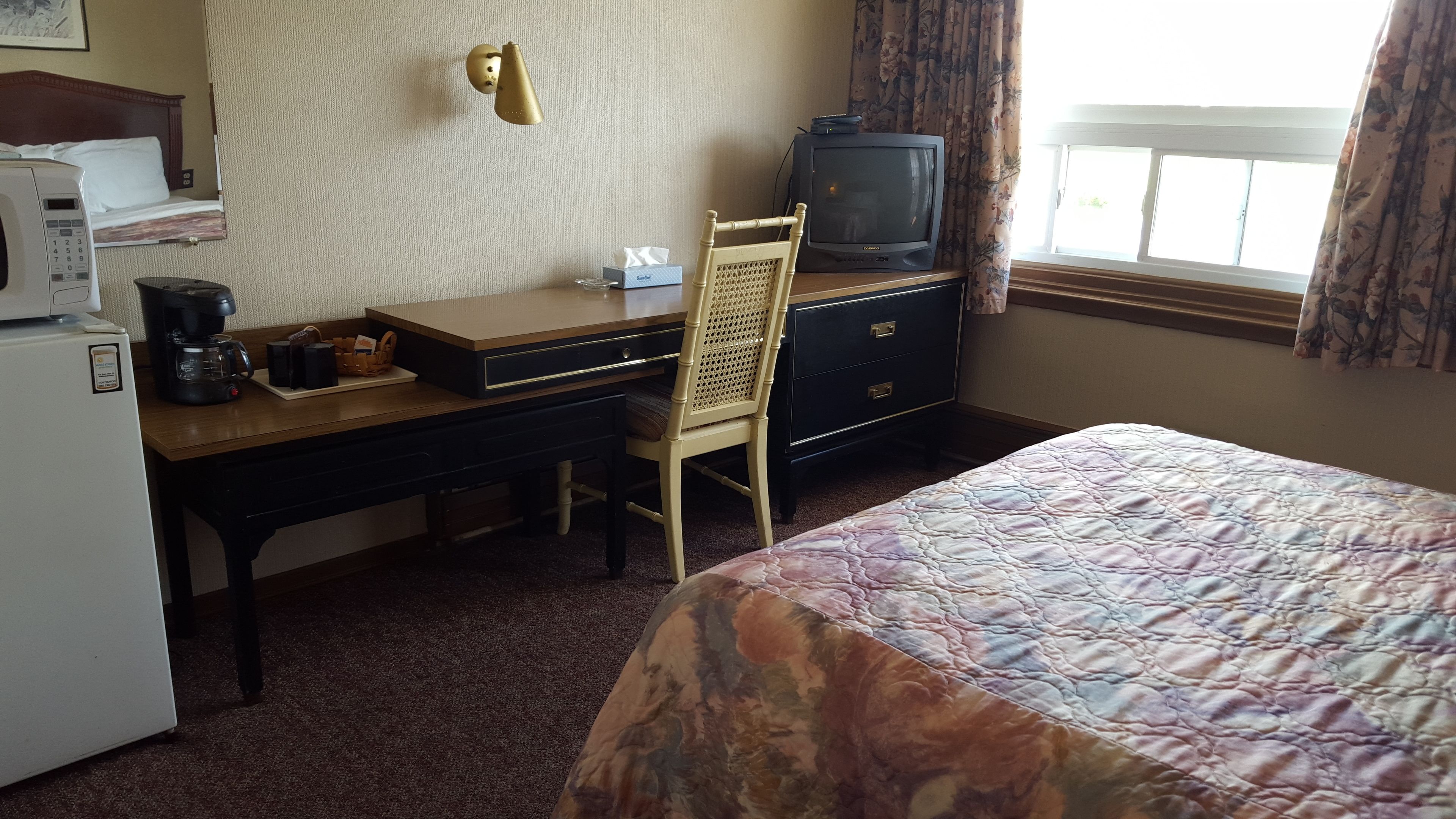 A hotel room with a bed, a desk with a computer, a chair, a television, and a coffee maker.