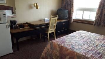 A hotel room with a bed, a desk with a computer, a chair, a television, and a coffee maker.