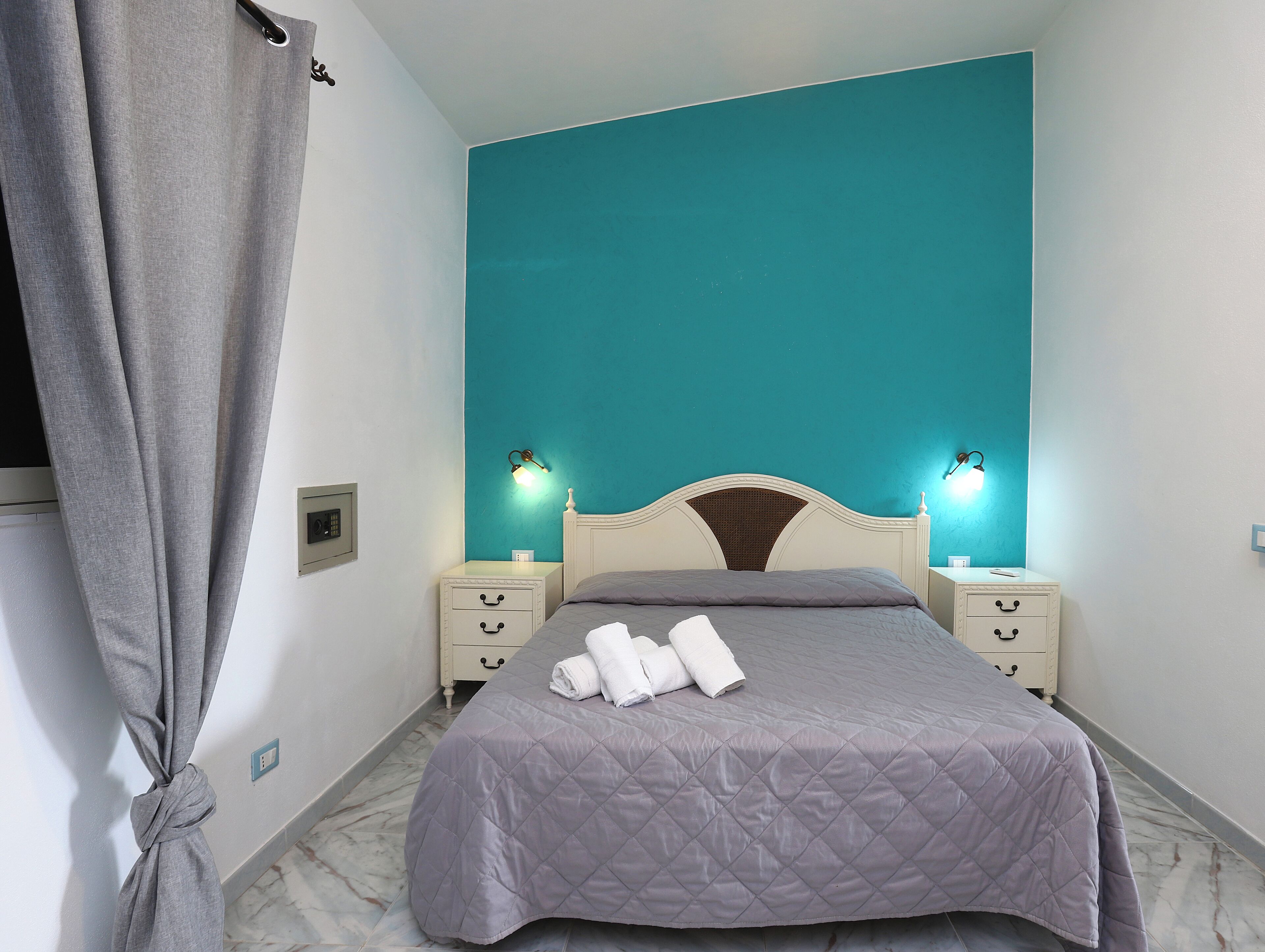 Ein Schlafzimmer mit einem Bett, zwei Nachttischen, einer Ablage und einer Wand in Türkis.