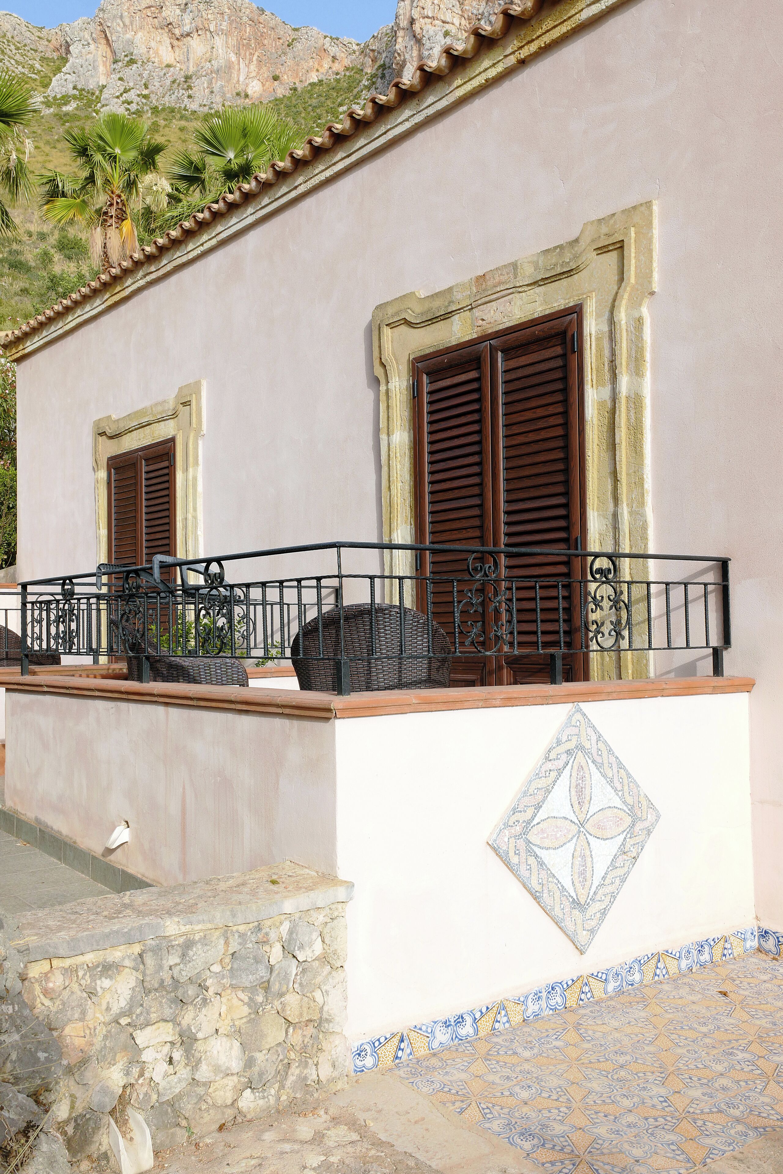 A building with a balcony, stone wall, and patterned floor tiles.