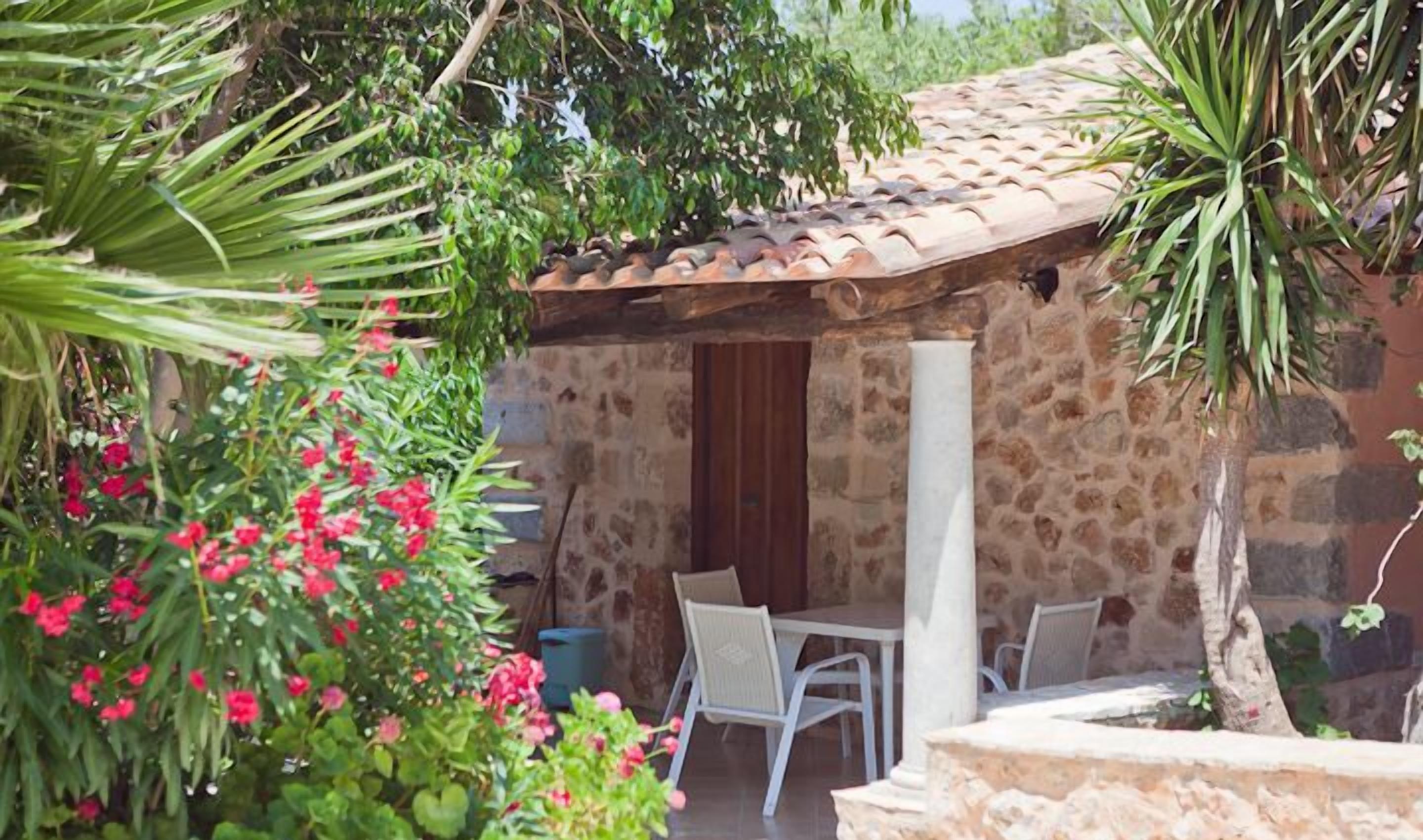 A stone building with a tiled roof, a wooden door, and a small patio with a table and chairs.