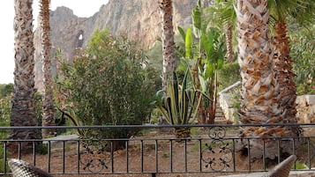 Una terraza con sillas de mimbre y vistas a palmeras y montañas rocosas.