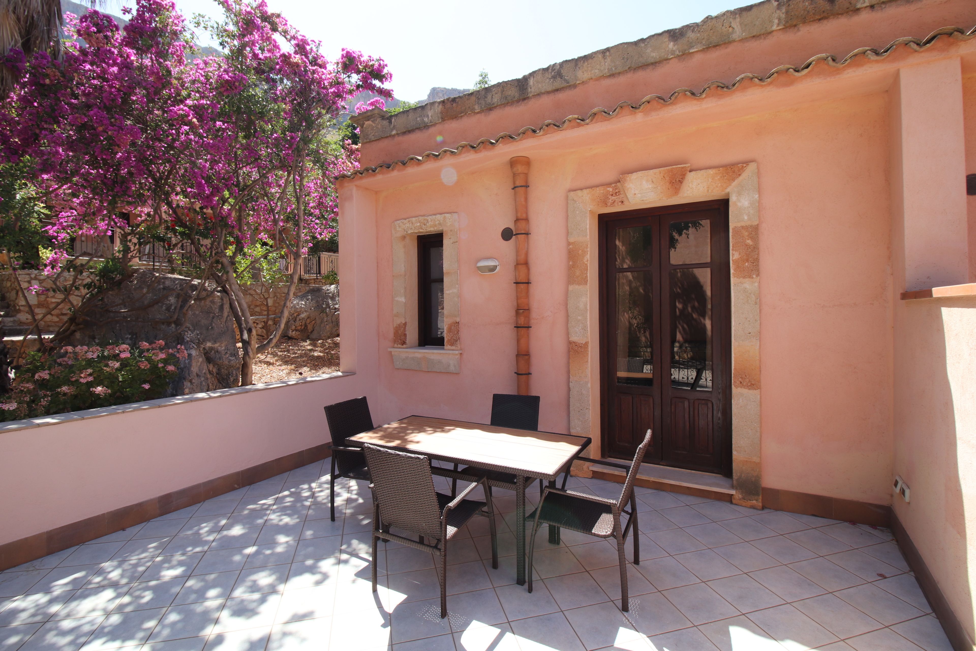 Eine Terrasse mit Tisch, Stühlen, einer Tür und einer rosa Wand.