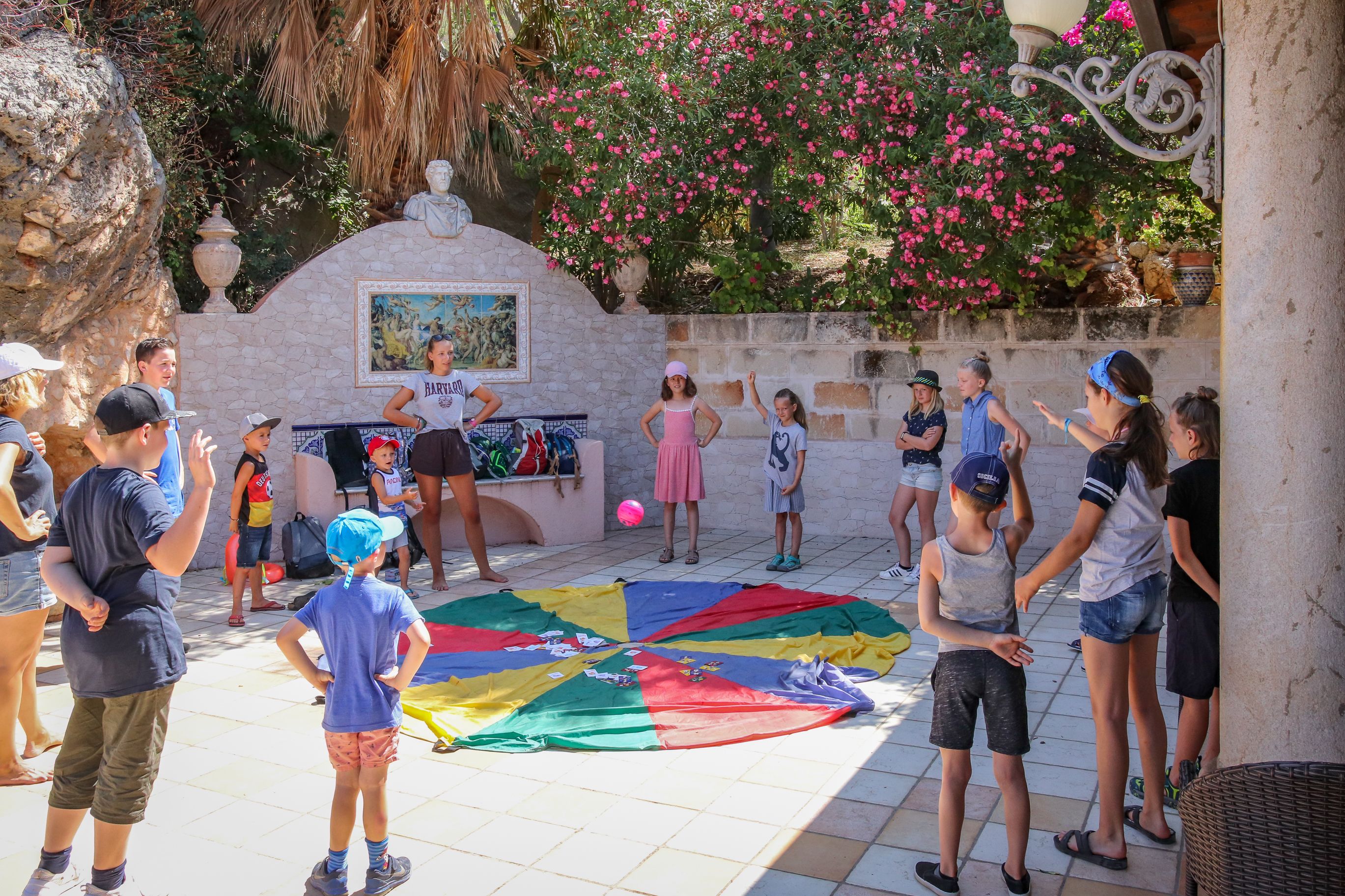 Un grupo de personas reunidas alrededor de una cometa colorida en un espacio al aire libre con paredes de piedra y un mural.