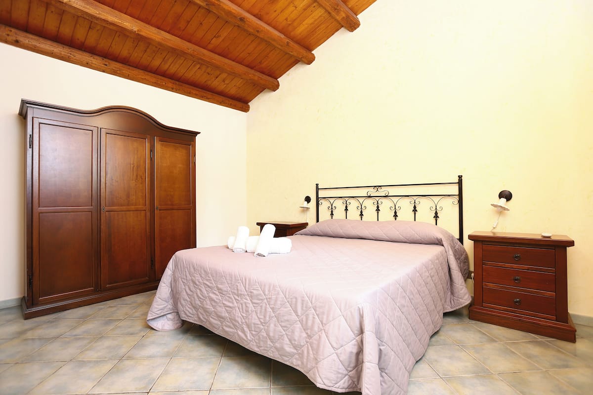 A bedroom with a bed, wooden wardrobe, and a nightstand.
