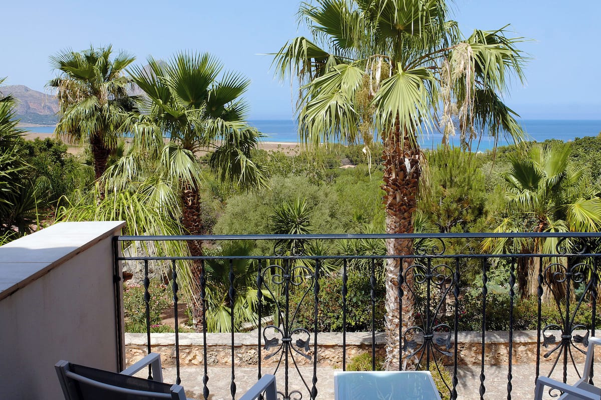 A balcony with a view of the sea, surrounded by palm trees and greenery.