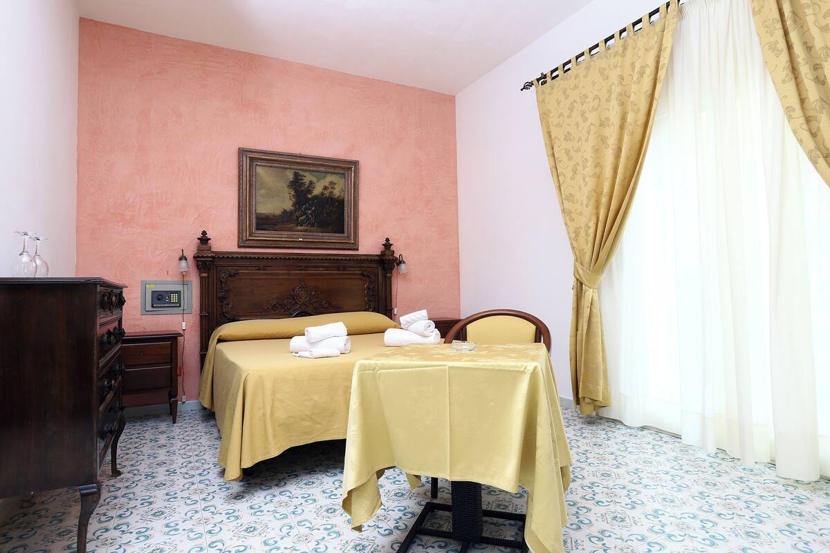 A room with a bed, a table, a dresser, and a painting on the wall.