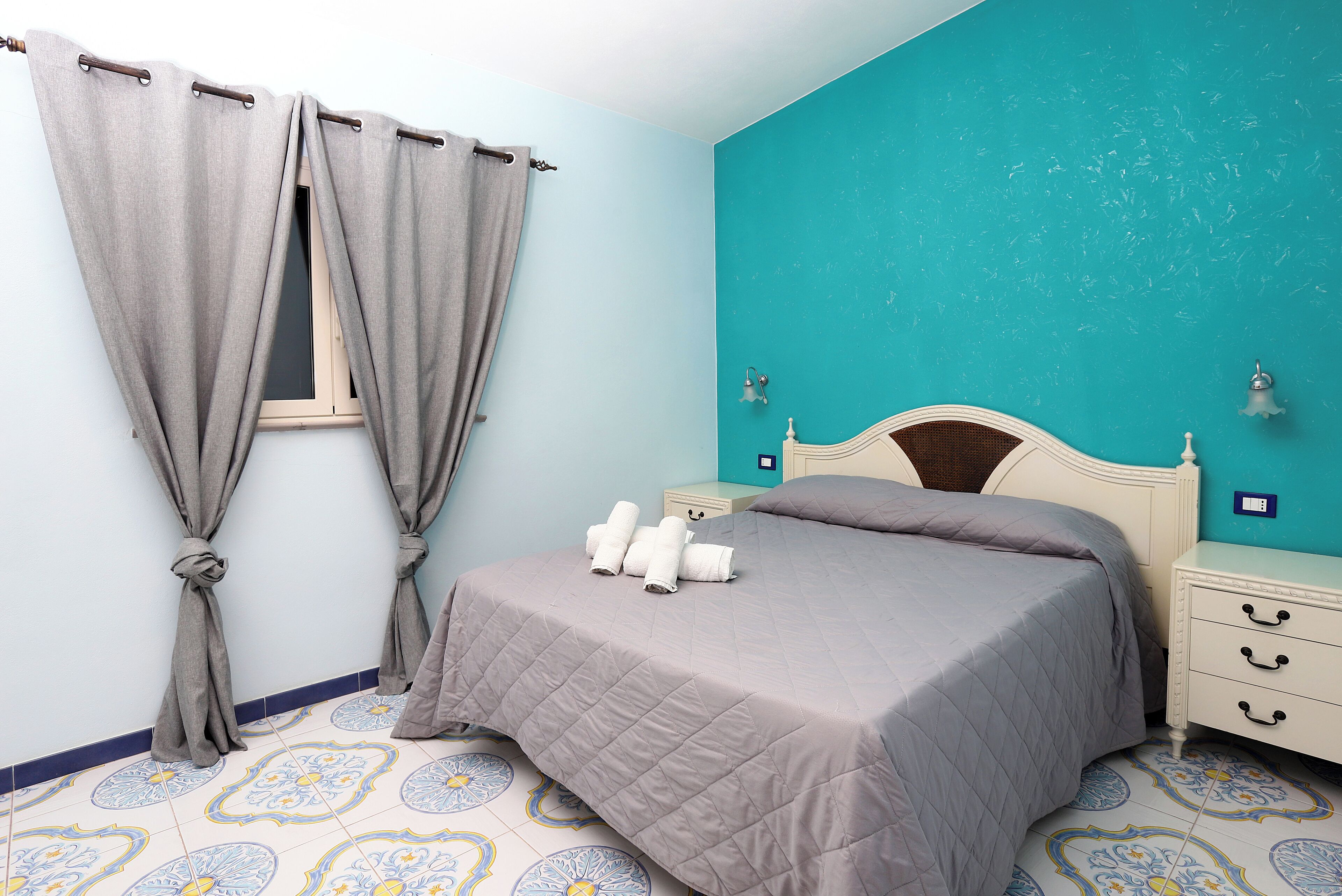 A bedroom with a bed, curtains, a nightstand, and a wall with a teal color.