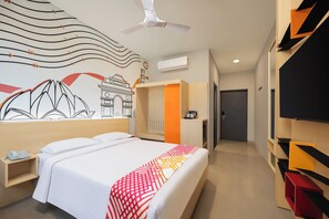 A hotel room with a bed, a nightstand, a ceiling fan, a wall-mounted TV, and a wardrobe. - Ginger East Delhi (New Delhi)