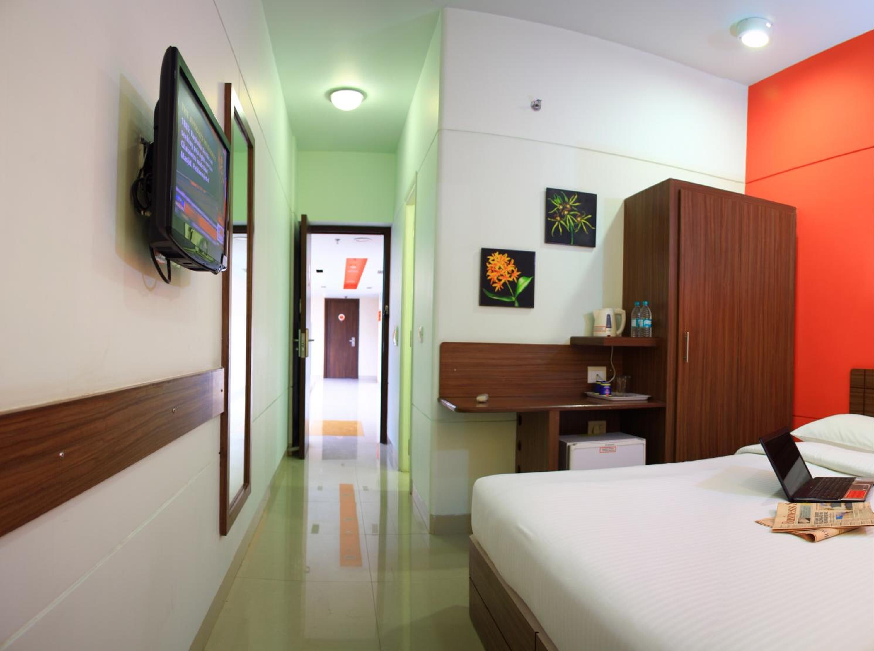 A hotel room with a bed, a desk with a laptop, a television on the wall, and artwork on the wall.