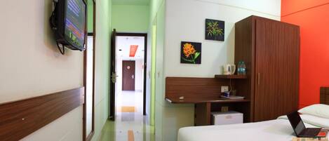 A hotel room with a bed, a desk with a laptop, a television on the wall, and artwork on the wall.