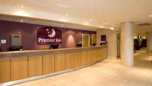 Un comptoir d’accueil d’hôtel avec une enseigne « Premier Inn », un bureau d’accueil et un sol carrelé.