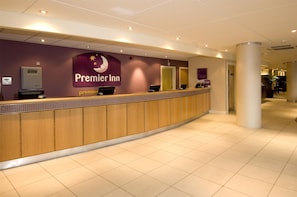 A hotel reception desk with a sign for Premier Inn, a reception counter, and a tiled floor. - Premier Inn Manchester M56/J6 Runger Lane South (Altrincham)