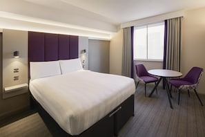 A hotel room with a bed, bedside tables, a desk, two chairs, and a window with curtains. - Premier Inn Manchester M56/J6 Runger Lane South (Altrincham)