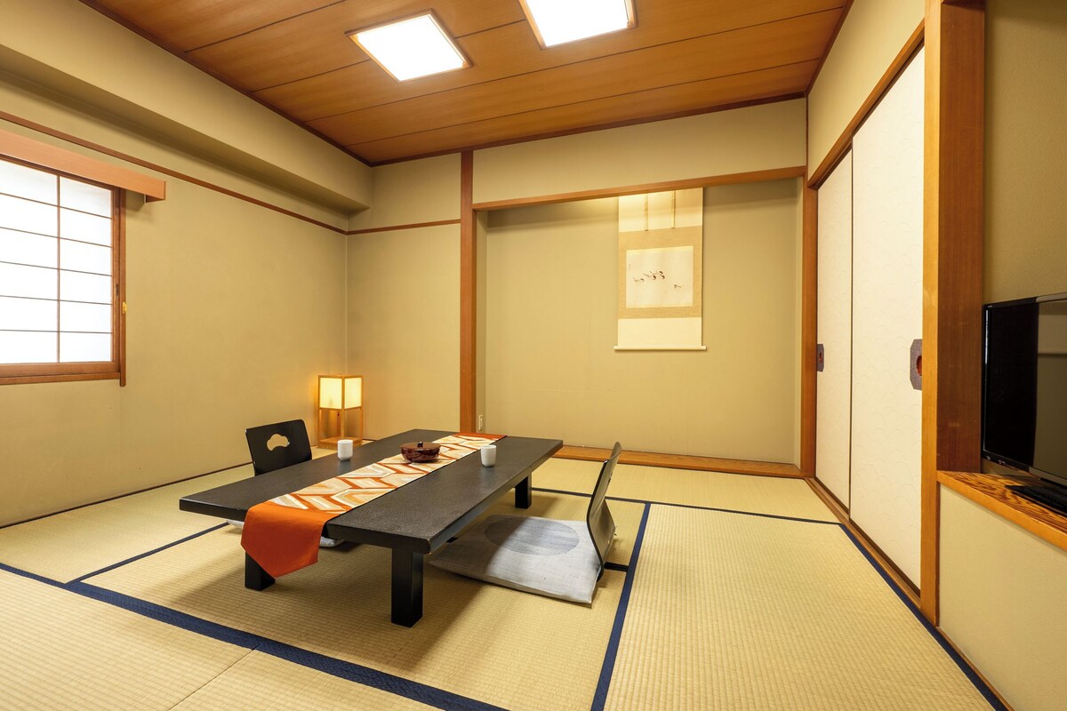Una stanza tradizionale giapponese con pavimento in tatami, un tavolino, un televisore e porte scorrevoli.